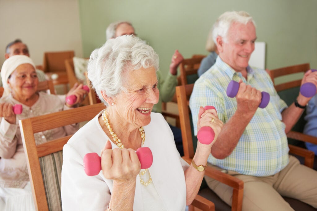 A group of seniors lifts weights while sitting.