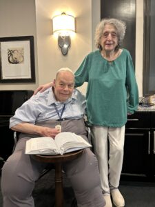 Man sitting and woman standing with table and open book