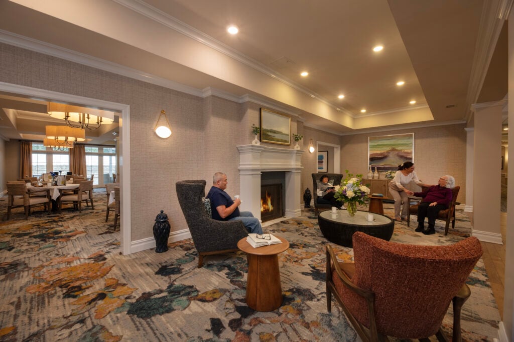 Two SLR Marlboro assisted living resident's and an associate sitting in the living room by a fire place.