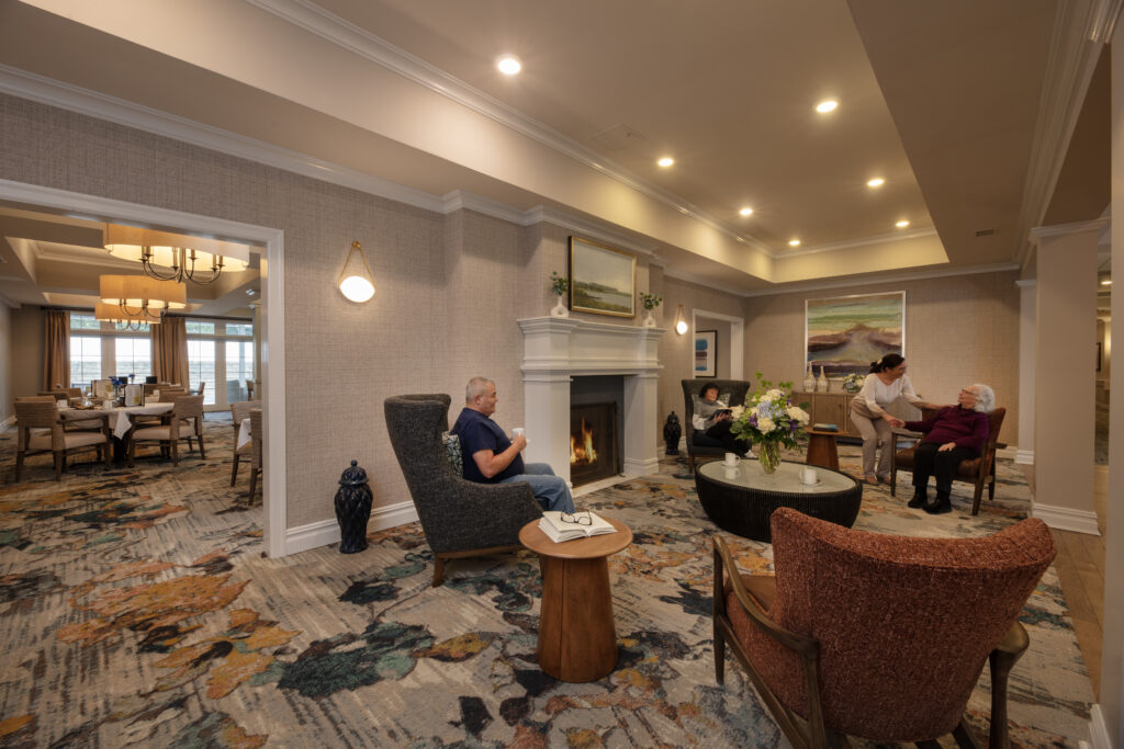 Two SLR Marlboro assisted living resident's and an associate sitting in the living room by a fire place.