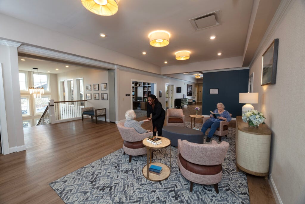 A second floor sitting area at SLR Marlboro assisted living with one resident reading, and the other talking to an associate.