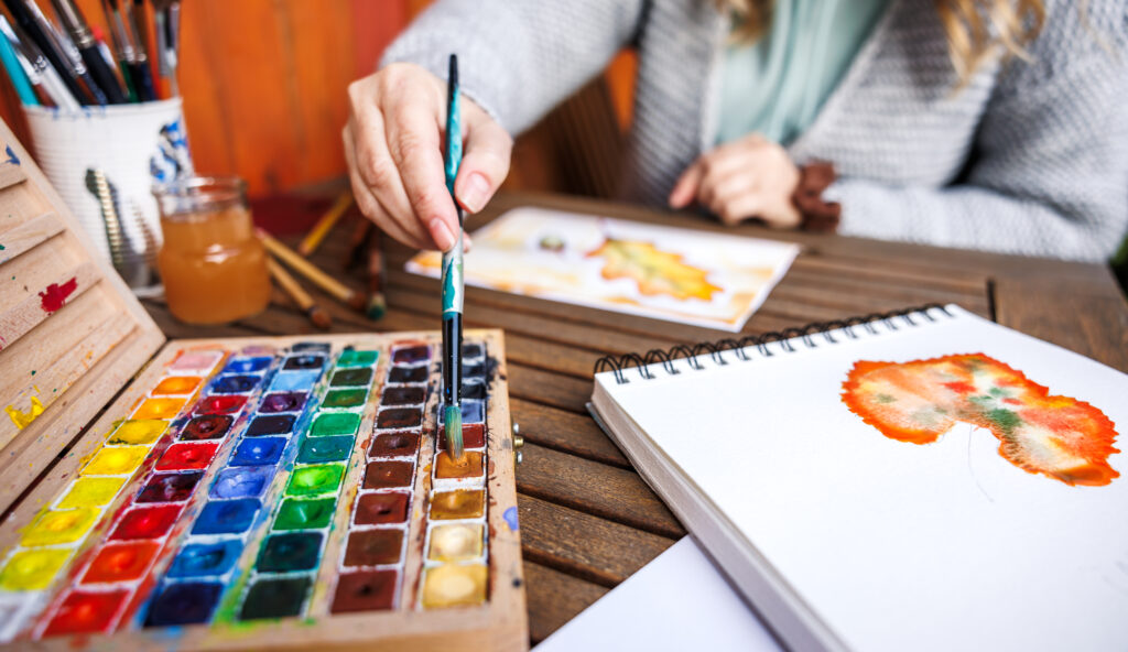 Watercolor painting. Woman artist dips paintbrush into color palette and painting a watercolor illustration