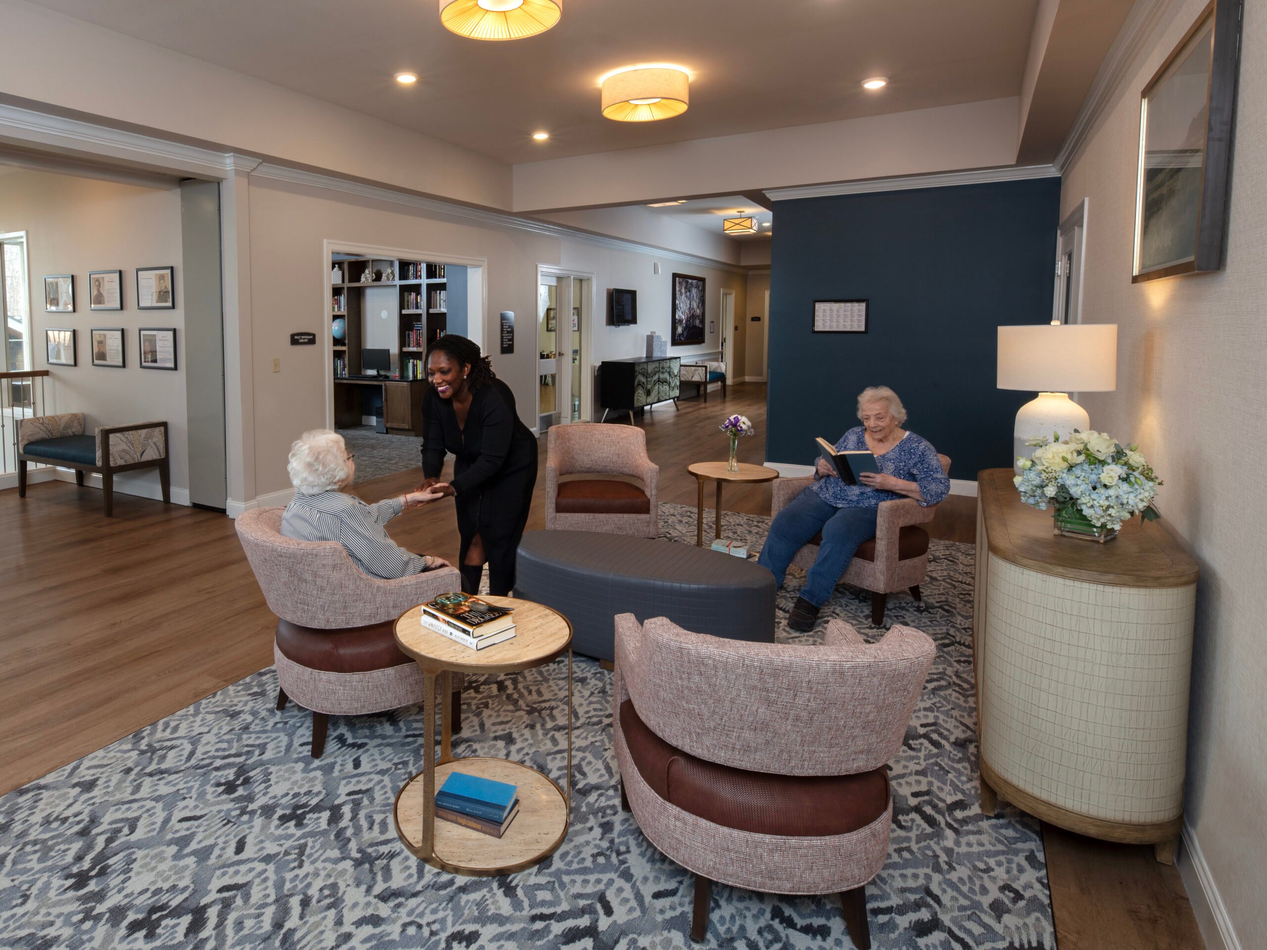 A second floor sitting area at SLR Marlboro assisted living with one resident reading, and the other talking to an associate.